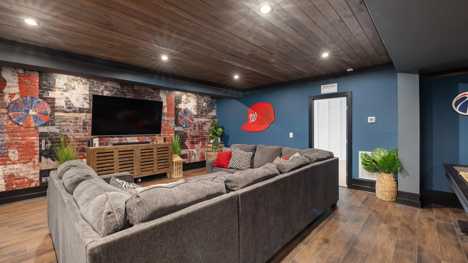 Finished basement lounge with wood plank ceiling and brick accent wall